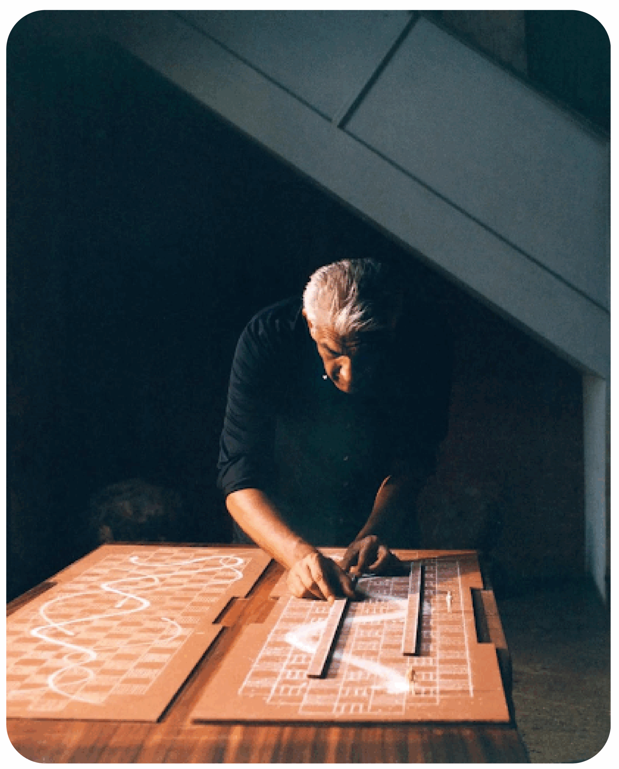 Under dramatic lighting, a designer meticulously arranges pieces on a scaled model of the Louis Vuitton Spring-Summer 2026 runway, showing the intricate planning process.