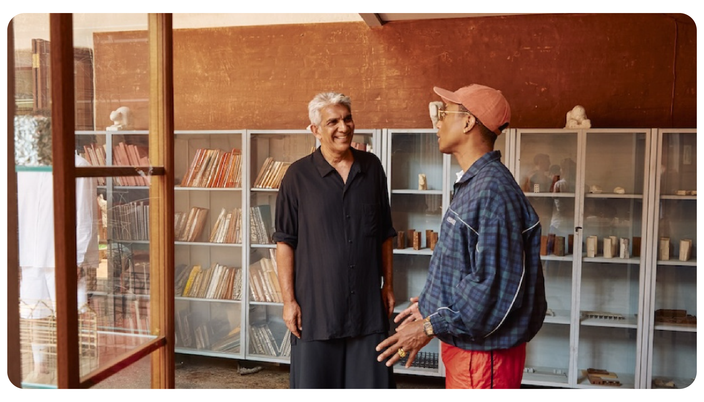 Pharrell Williams, creative director of Louis Vuitton menswear, in a collaborative discussion with a designer in a creative studio filled with books and architectural models.